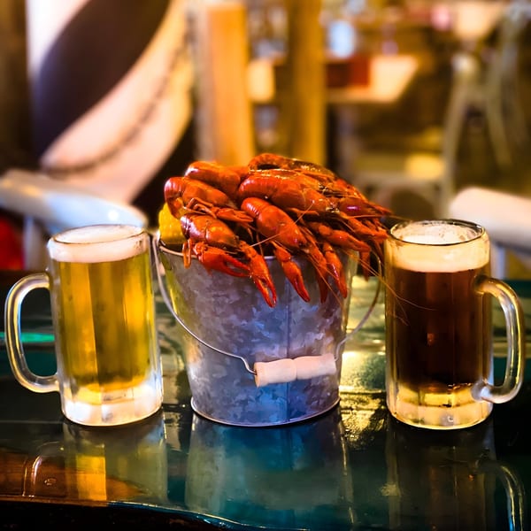 A bucket of red crawfish and corn on the cob, flanked by two mugs of beer.