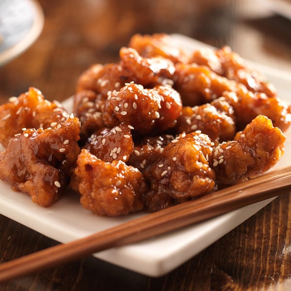 Close-up of Crab Fever's sesame chicken with a sweet glaze and chopsticks on a white plate.