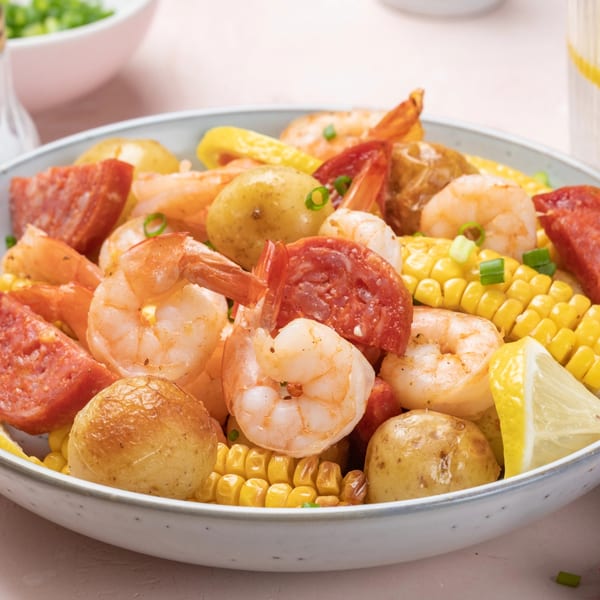 Close-up of a seafood boil with shrimp, potatoes, corn, and sausage in a white bowl.
