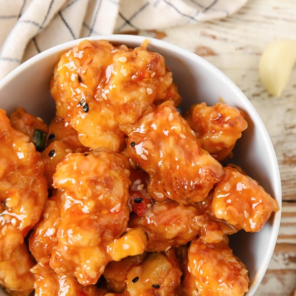 Close-up of golden fried shrimp coated in sweet chili sauce with sesame seeds in a white bowl.