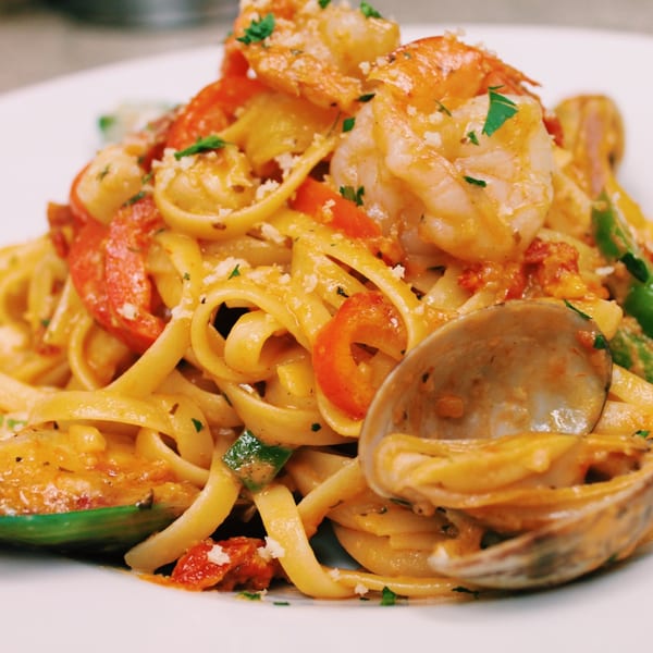 Seafood linguine with shrimp, clams, mussels, red peppers, and parmesan cheese on a white plate.